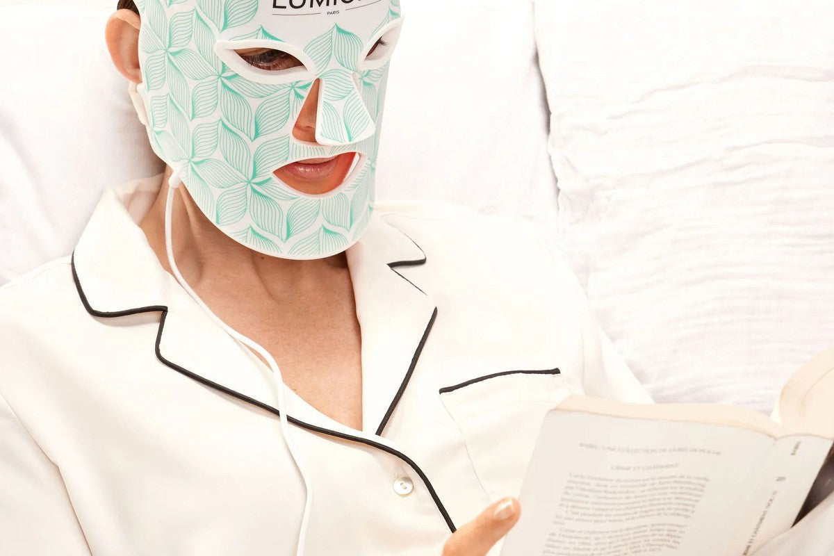 Woman reading in bed during a ten-minute LED face mask session